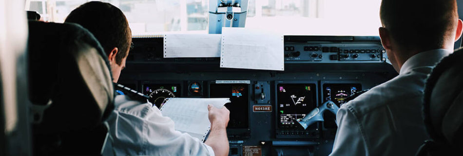 Two airline pilots seated in a flight deck, with one reviewing flight paperwork.